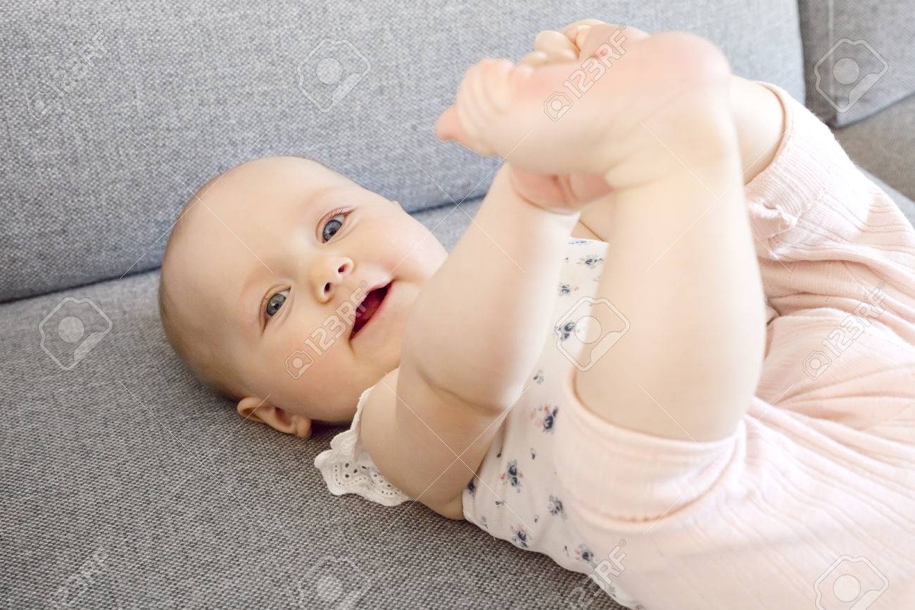 Cute And Happy Baby Girl With Blue Eyes Laying On The Sofa Holding Her Foot Looking Into Camera Stock Photo Picture And Royalty Free Image Image