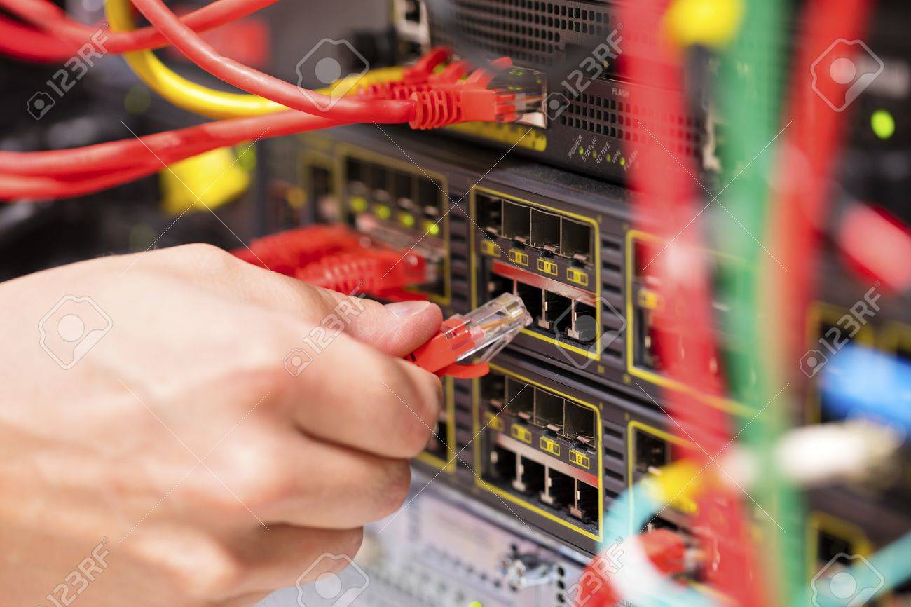 IT technician or engineer connects a gigabit network cable into switch in datacenter - 63796637 IT technician or engineer connects a gigabit network cable into switch in datacenter - 63796637