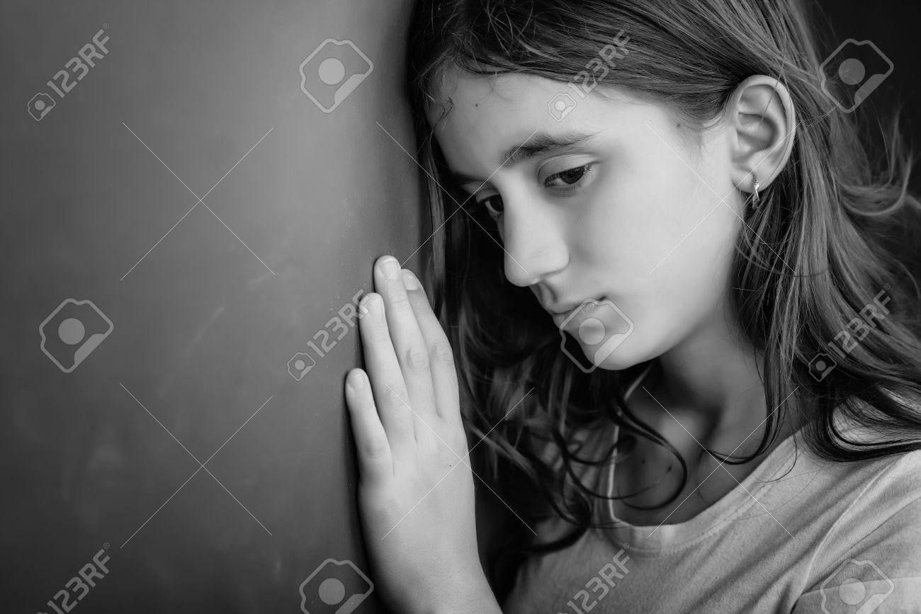 Grunge black and white portrait of a sad girl leaning against a wall stock photo