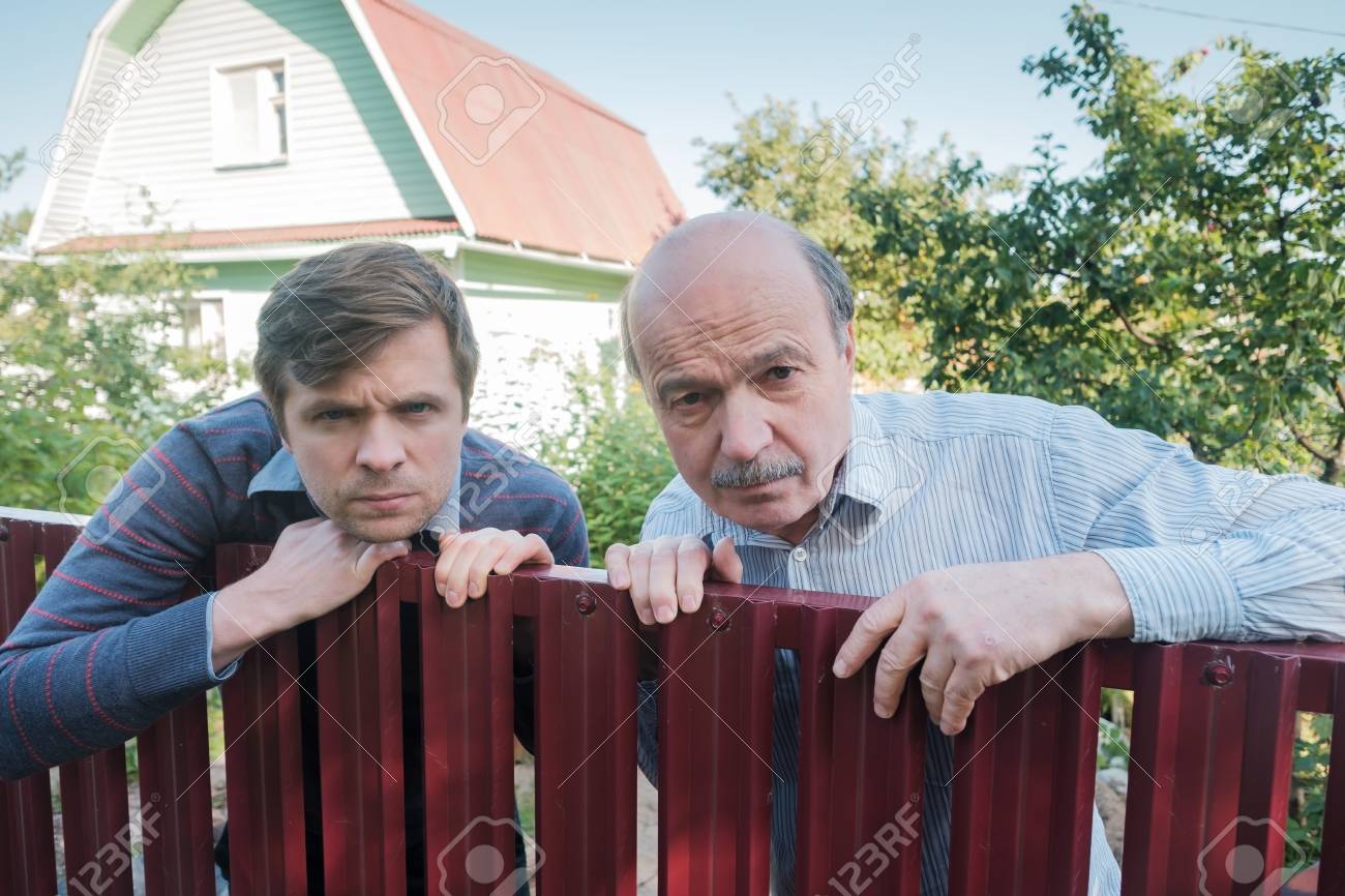 two angry caucasian men carefully watching over the fence. Concept of curious neighbors and private life - 114423063 two angry caucasian men carefully watching over the fence. Concept of curious neighbors and private life - 114423063