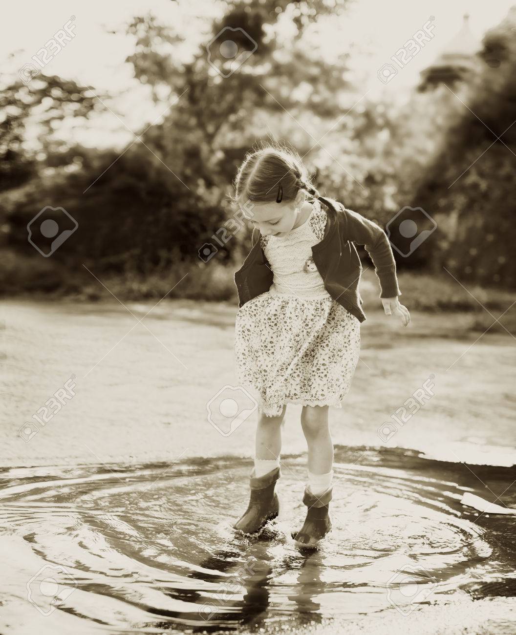 赤い雨を着てかわいい女の子ブーツ水たまりに飛び込む の写真素材 画像素材 Image