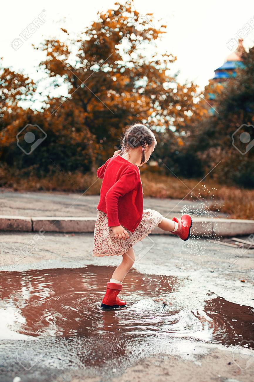 赤い雨を着てかわいい女の子ブーツ水たまりに飛び込む の写真素材 画像素材 Image