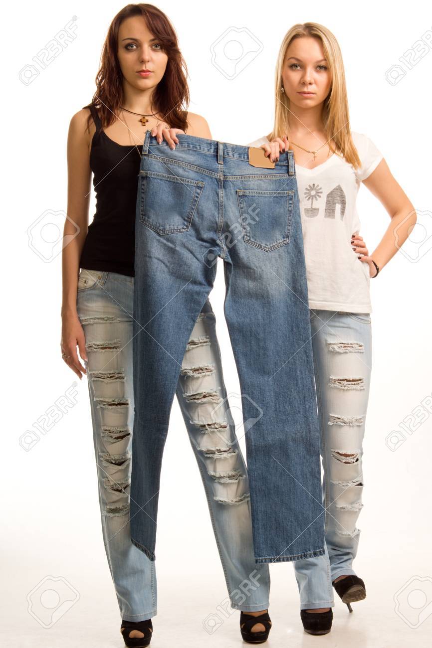 Chicas Jóvenes Con Expresiones Sensuales Que Presentan En Sus Pantalones Vaqueros De Diseño Moderno Con Agujeros Sosteniendo Un Par De Simples Jeans Que Se Han Fighing Más Aislado En Blanco Fotos,