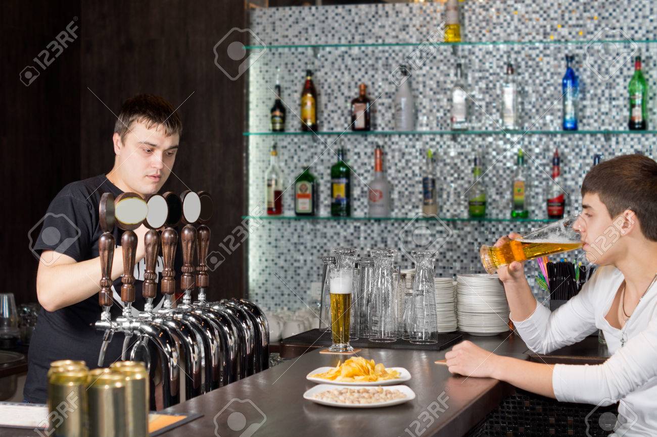 若い男性客ながら調剤のドラフト ビールを作業バーテンダー ナイトクラブやバーのカウンターで 1 パイントを飲む の写真素材 画像素材 Image