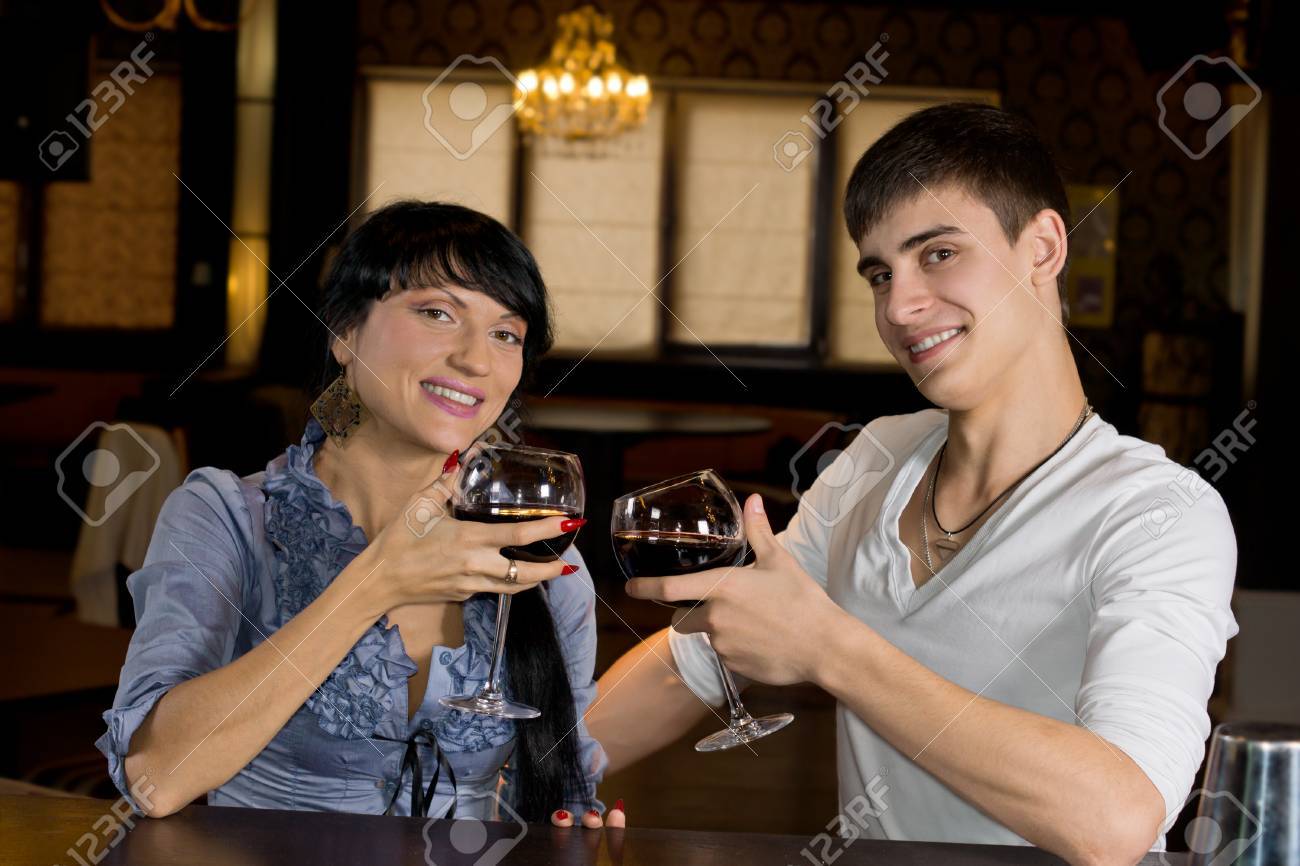 魅力的な若いカップル彼らは乾杯のグラスを上げるし カメラに笑顔のバーでポーズ の写真素材 画像素材 Image