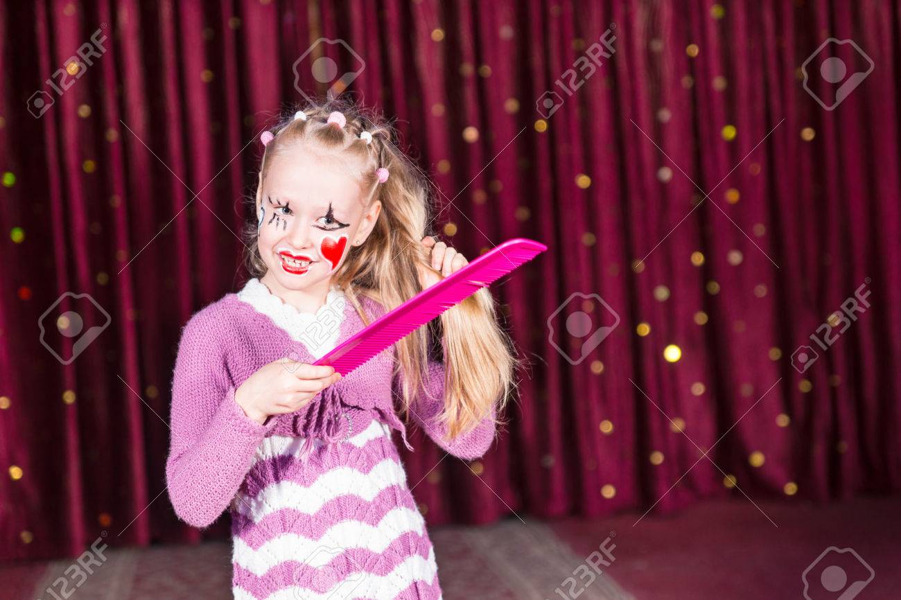 ピンクのパントマイムのかなり若い女の子彼女のカラフルなメイクアップで特大櫛で長いブロンドの髪をとかすステージに立っての衣装し 塗料に直面 の写真素材 画像素材 Image