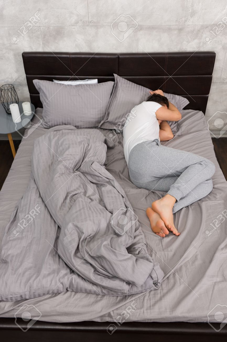 Young Tired Man In Pajama Sleeping Without Blanket In Stylish Bed