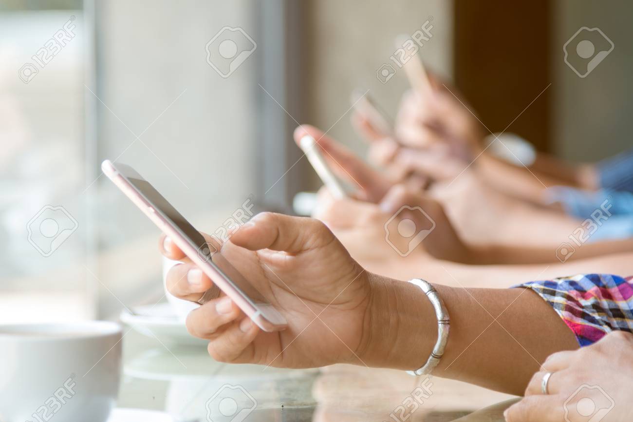 Close up of four people hand holding mobile phone and using internet in coffee shop with warm light flare - 84528317 Close up of four people hand holding mobile phone and using internet in coffee shop with warm light flare - 84528317