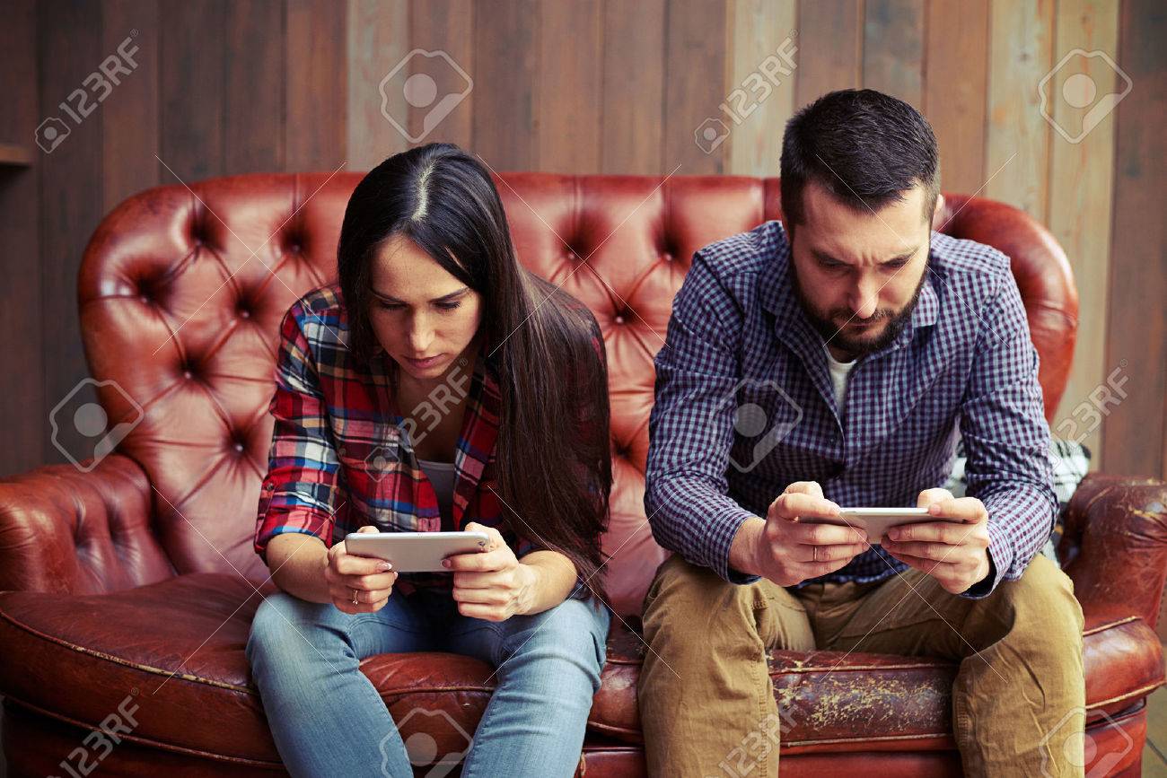 concept photo of smartphone addiction. young woman and man sitting on the sofa with smartphone and do not looking at each other - 54207353 concept photo of smartphone addiction. young woman and man sitting on the sofa with smartphone and do not looking at each other - 54207353