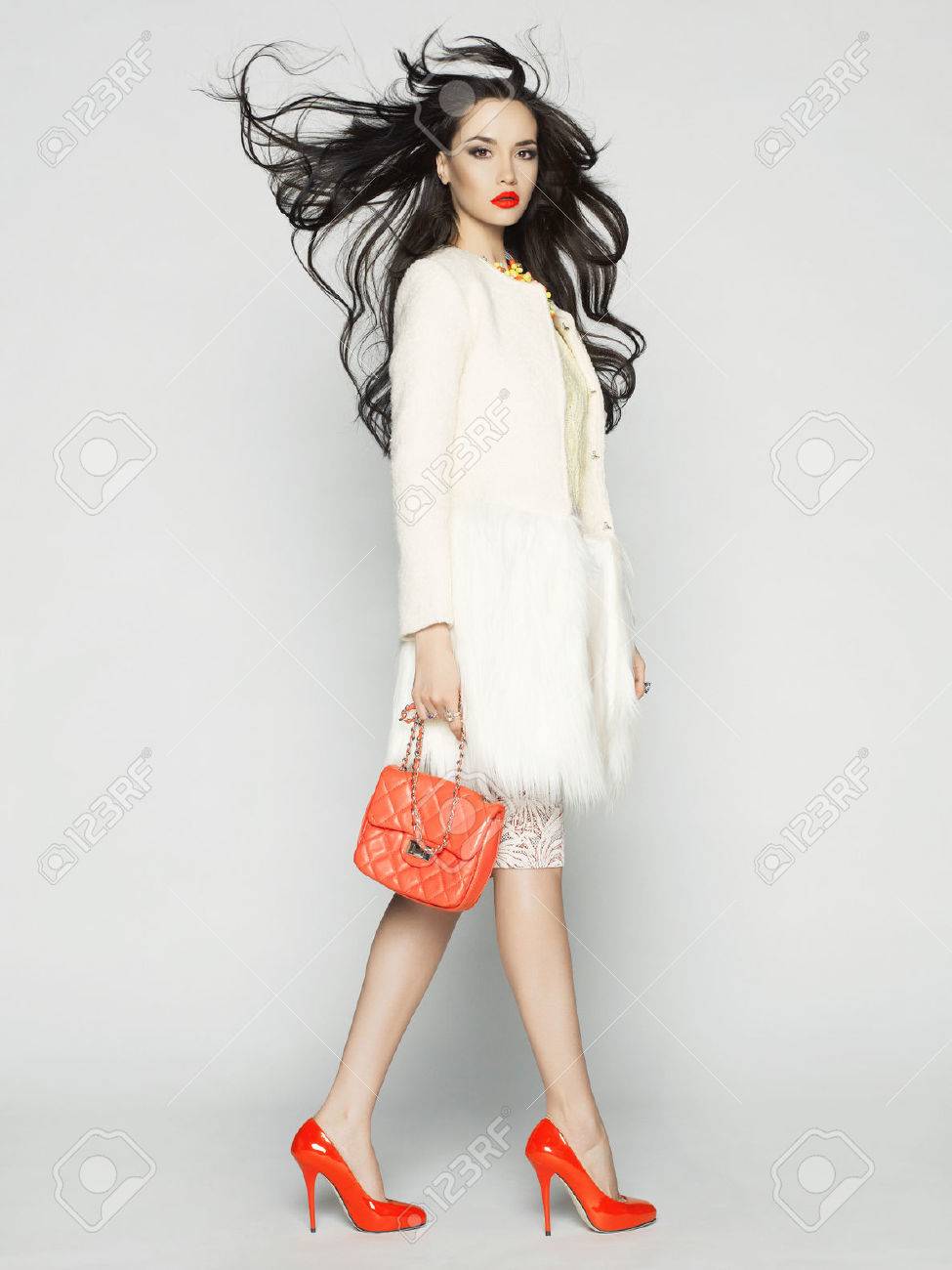 スタジオでポーズのファッションの服の美しいブルネットのモデル コート ハンドバッグ 赤い靴を身に着けています の写真素材 画像素材 Image