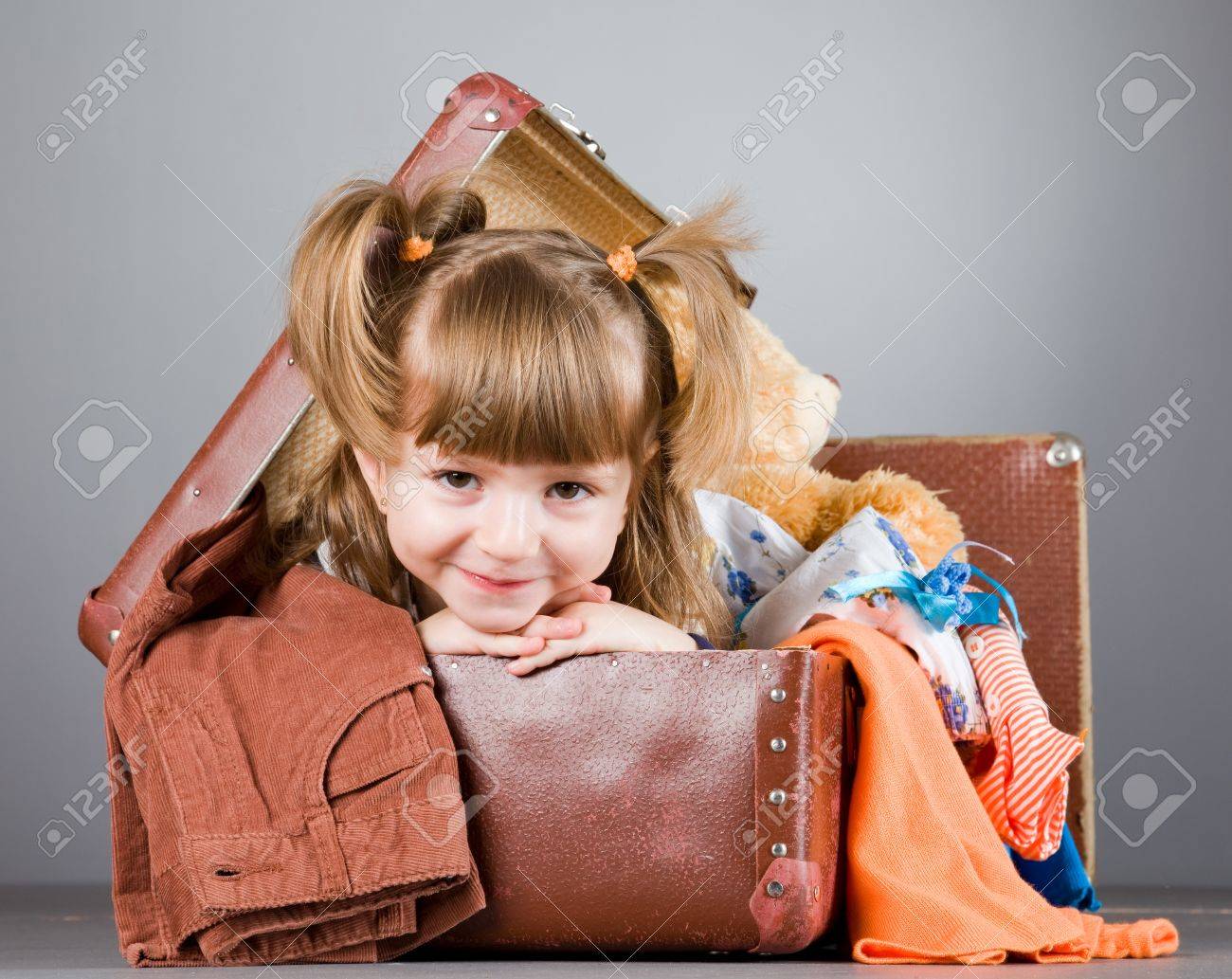 4 歳の女の子は喜んでおもちゃや服を着て古いスーツケースに座っています の写真素材 画像素材 Image