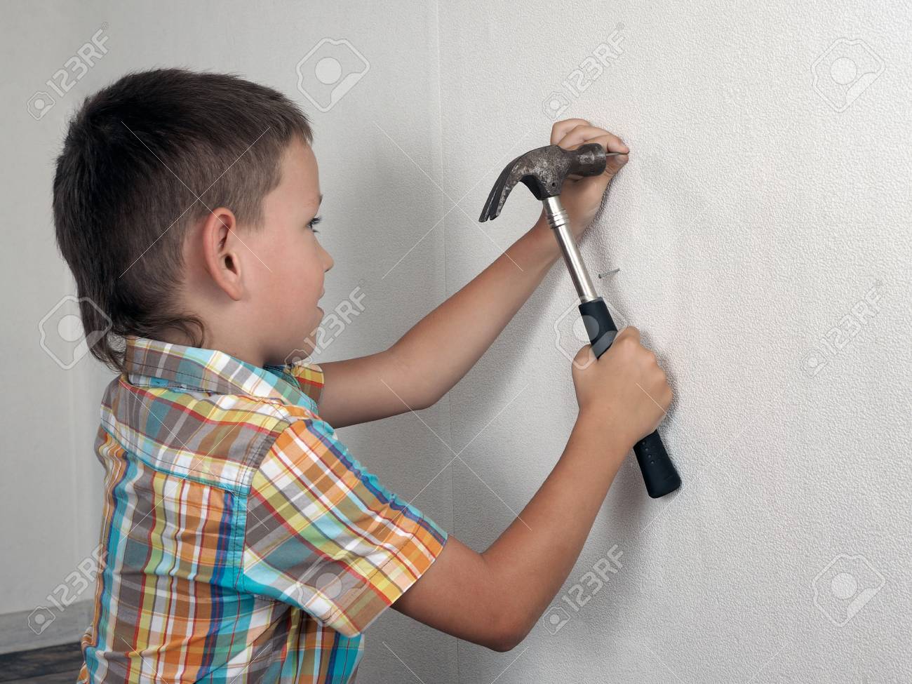 Little Boy Is Hammering A Nail Into The Wall With A Hammer. Funny Child 6 Years Old Helps In Repairing A New Family Home. Baby With Nails And A Hammer Stock Photo, Little Boy Is Hammering A Nail Into The Wall With A Hammer. Funny Child 6 Years Old Helps In Repairing A New Family Home. Baby With Nails And A Hammer Stock Photo,