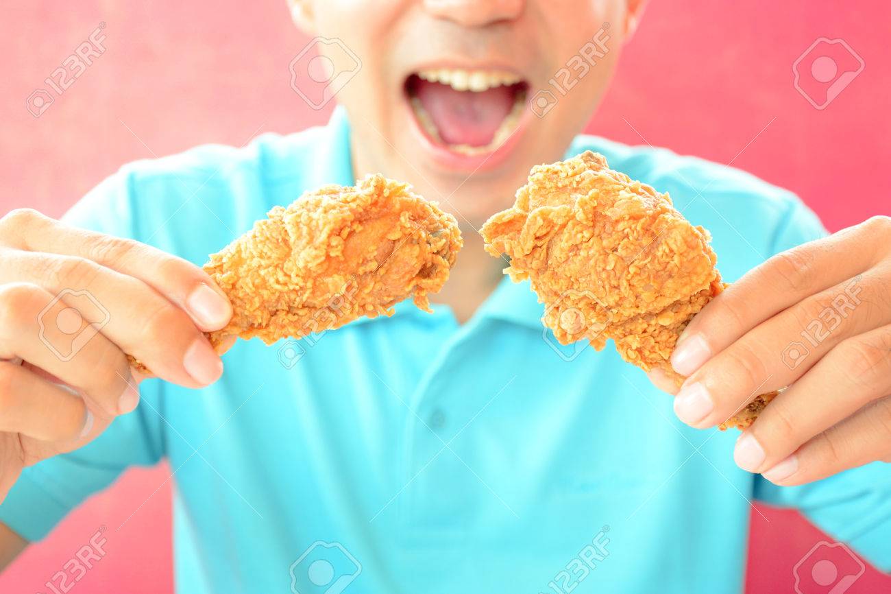 フライド チキンの足またはばち状核突起を食べて口を開いてを持つ男 の写真素材 画像素材 Image