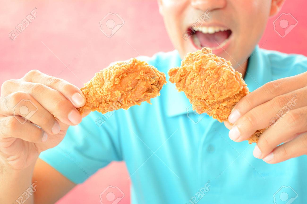 フライド チキンの足またはばち状核突起を食べて口を開いてを持つ男 の写真素材 画像素材 Image