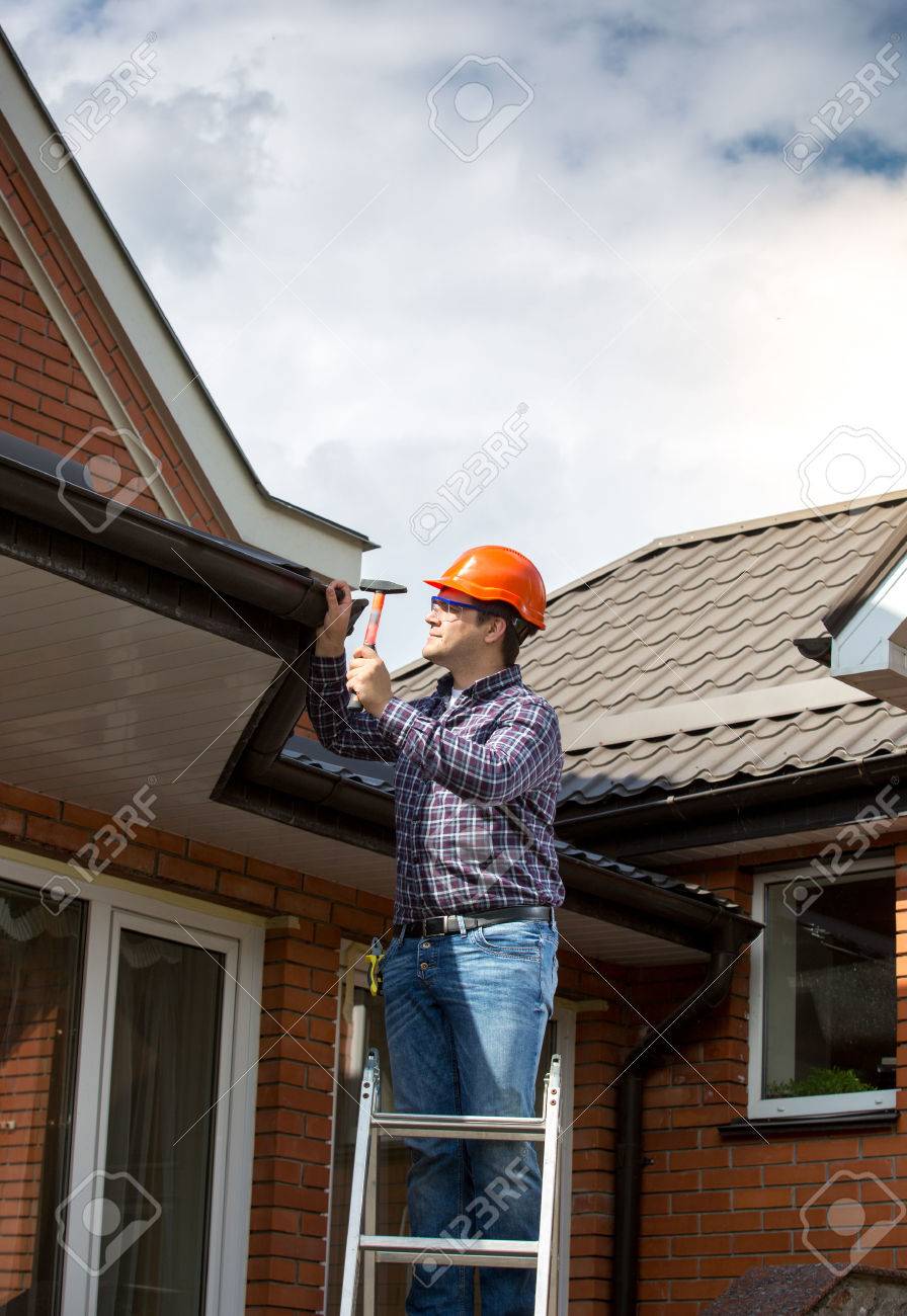 Professional carpenter standing on high ladder and repairing house roof - 41600650 Professional carpenter standing on high ladder and repairing house roof - 41600650