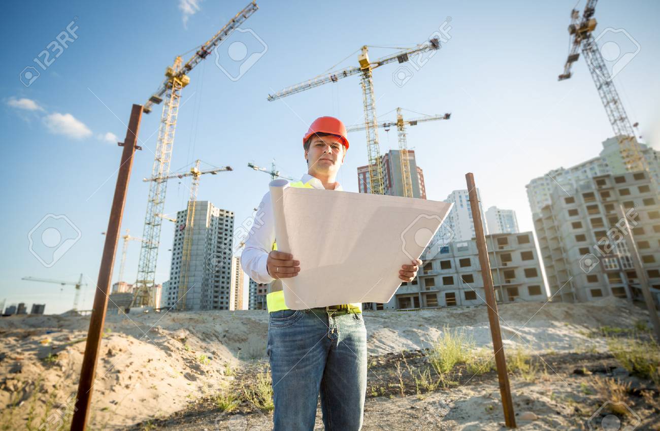 Construction engineer in hardhat inspecting blueprints on building site - 41681533 Construction engineer in hardhat inspecting blueprints on building site - 41681533