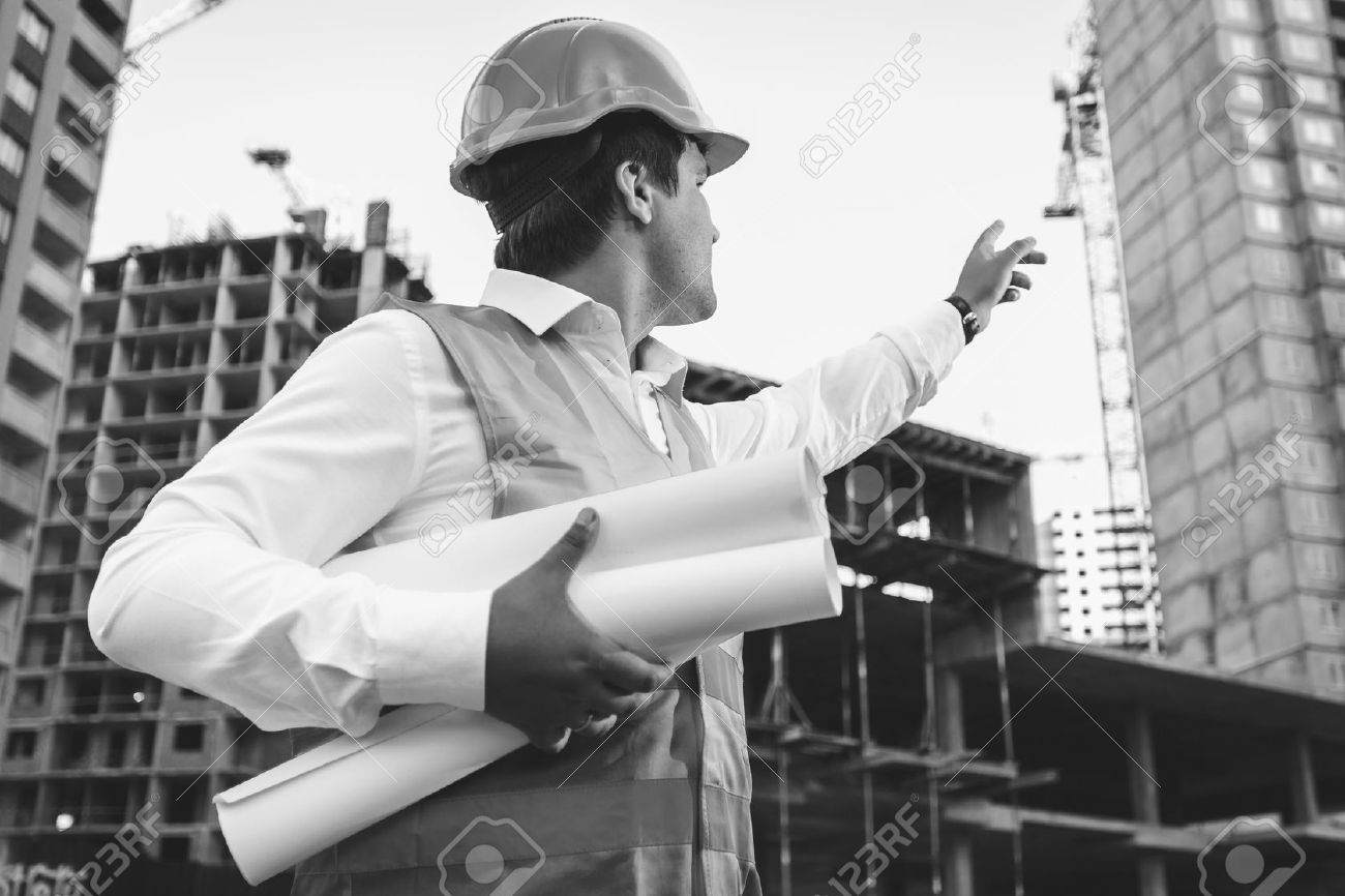 Black and white closeup photo of engineer with blueprints checking building site construction - 41681593 Black and white closeup photo of engineer with blueprints checking building site construction - 41681593