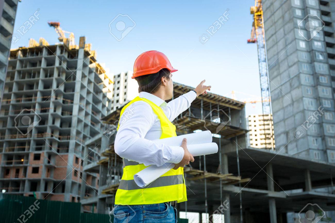 Site manager in hardhat pointing at crane on building site - 41681675 Site manager in hardhat pointing at crane on building site - 41681675