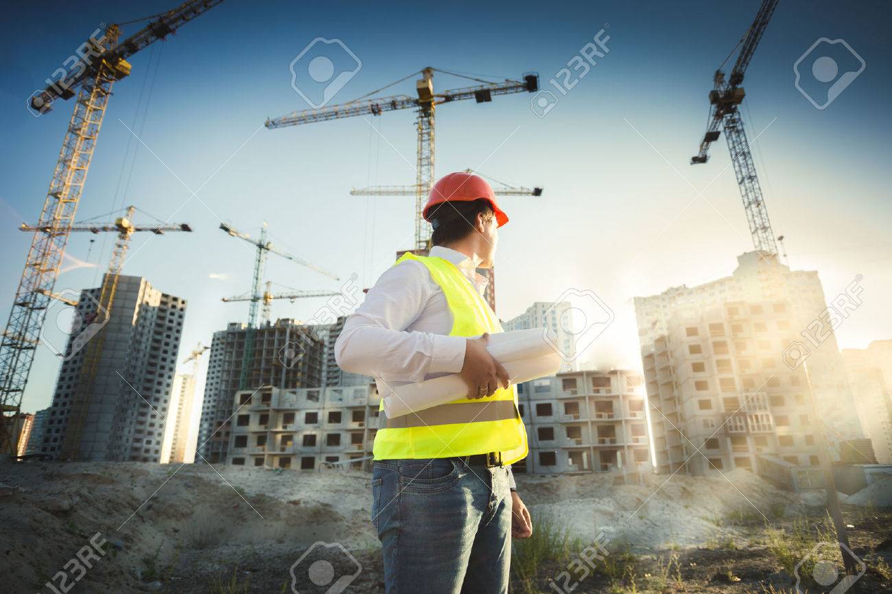 Man in hardhat and green jacket posing on building site at sunset - 41681756 Man in hardhat and green jacket posing on building site at sunset - 41681756