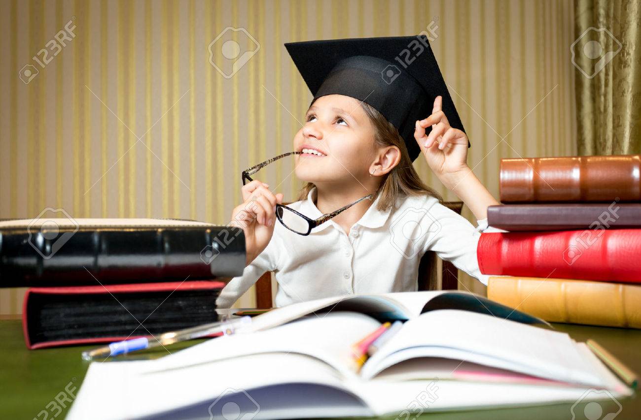 Portrait of smart thoughtful girl posing at desk in graduation cap - 43406719 Portrait of smart thoughtful girl posing at desk in graduation cap - 43406719