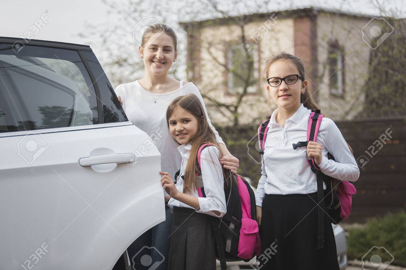 Portrait of happy mother and two girls with school bags posing at the car - 57265174 Portrait of happy mother and two girls with school bags posing at the car - 57265174