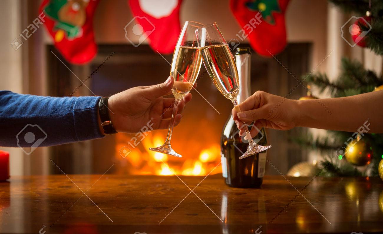 Closeup of man and woman celebrating Christmas and clinking glasses with champagne at fireplace - 65303364 Closeup of man and woman celebrating Christmas and clinking glasses with champagne at fireplace - 65303364