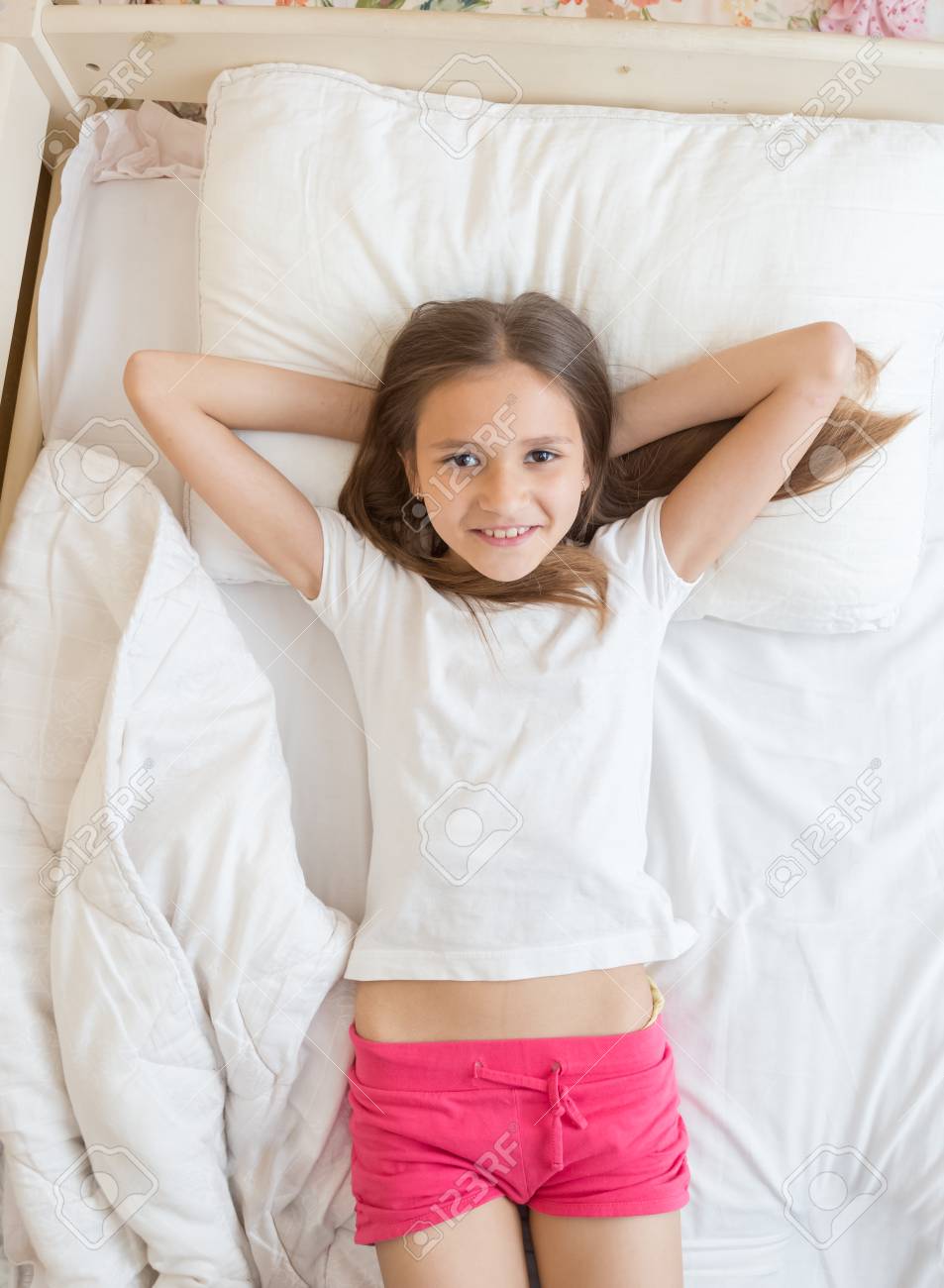 ベッドに横たわってカメラで見上げる幸せな笑顔の女の子の高いポイント