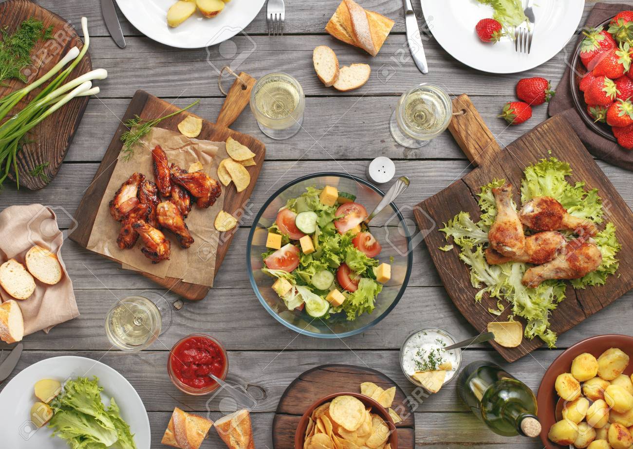 Different food cooked on the grill on a wooden table, grilled chicken legs, buffalo wings, salad, potatoes, bottle of wine and three glasses of wine and strawberry. - 60233284 Different food cooked on the grill on a wooden table, grilled chicken legs, buffalo wings, salad, potatoes, bottle of wine and three glasses of wine and strawberry. - 60233284