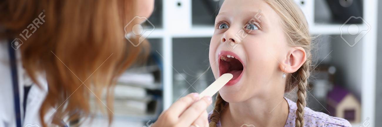 A small little child on a doctor's examination, ENT looks at his throat with a disposable wooden stick, mendalins, inflammation and sore throat can cause heat. nose and throat - 87287125 A small little child on a doctor's examination, ENT looks at his throat with a disposable wooden stick, mendalins, inflammation and sore throat can cause heat. nose and throat - 87287125