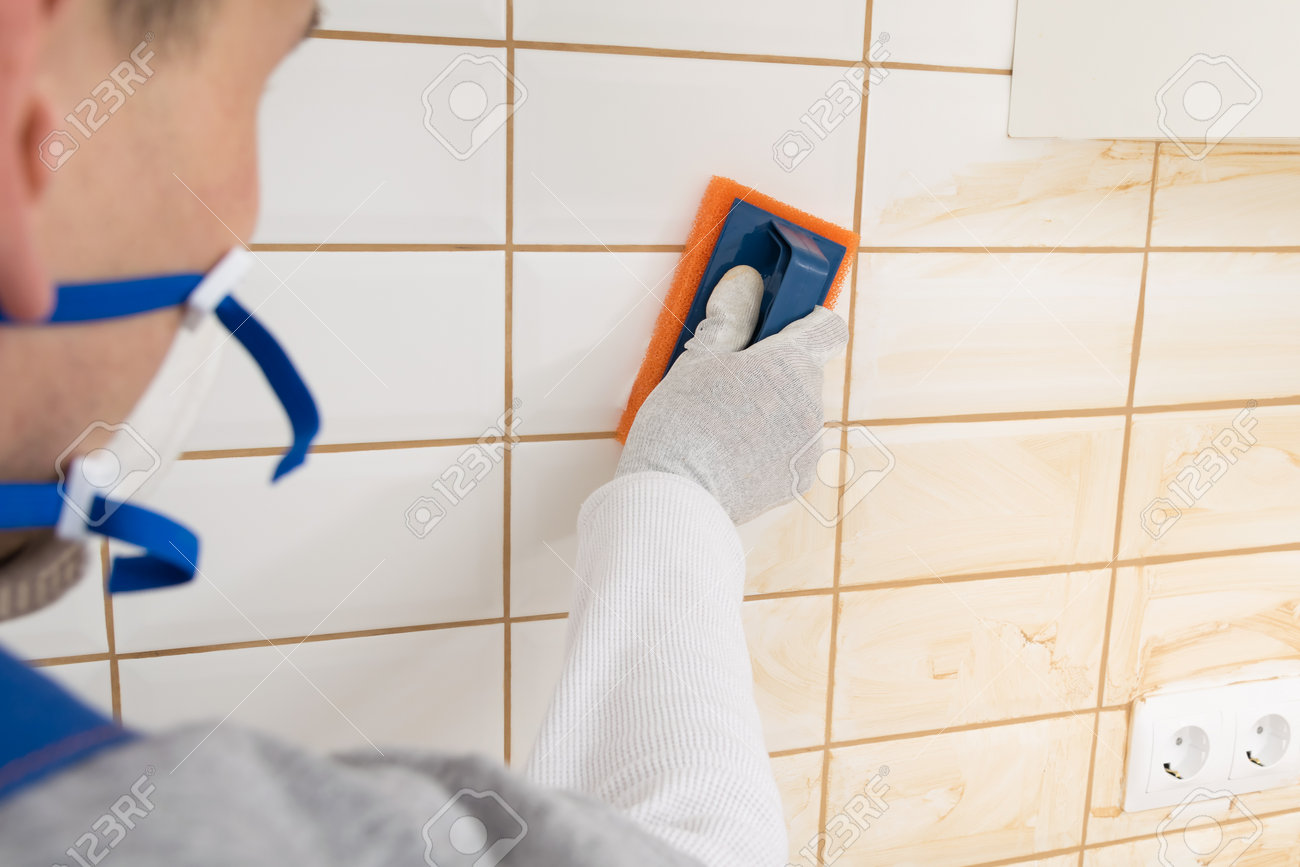 the master rubs the brown grout on white tiles with a special sponge, finishing work - 169144062 the master rubs the brown grout on white tiles with a special sponge, finishing work - 169144062