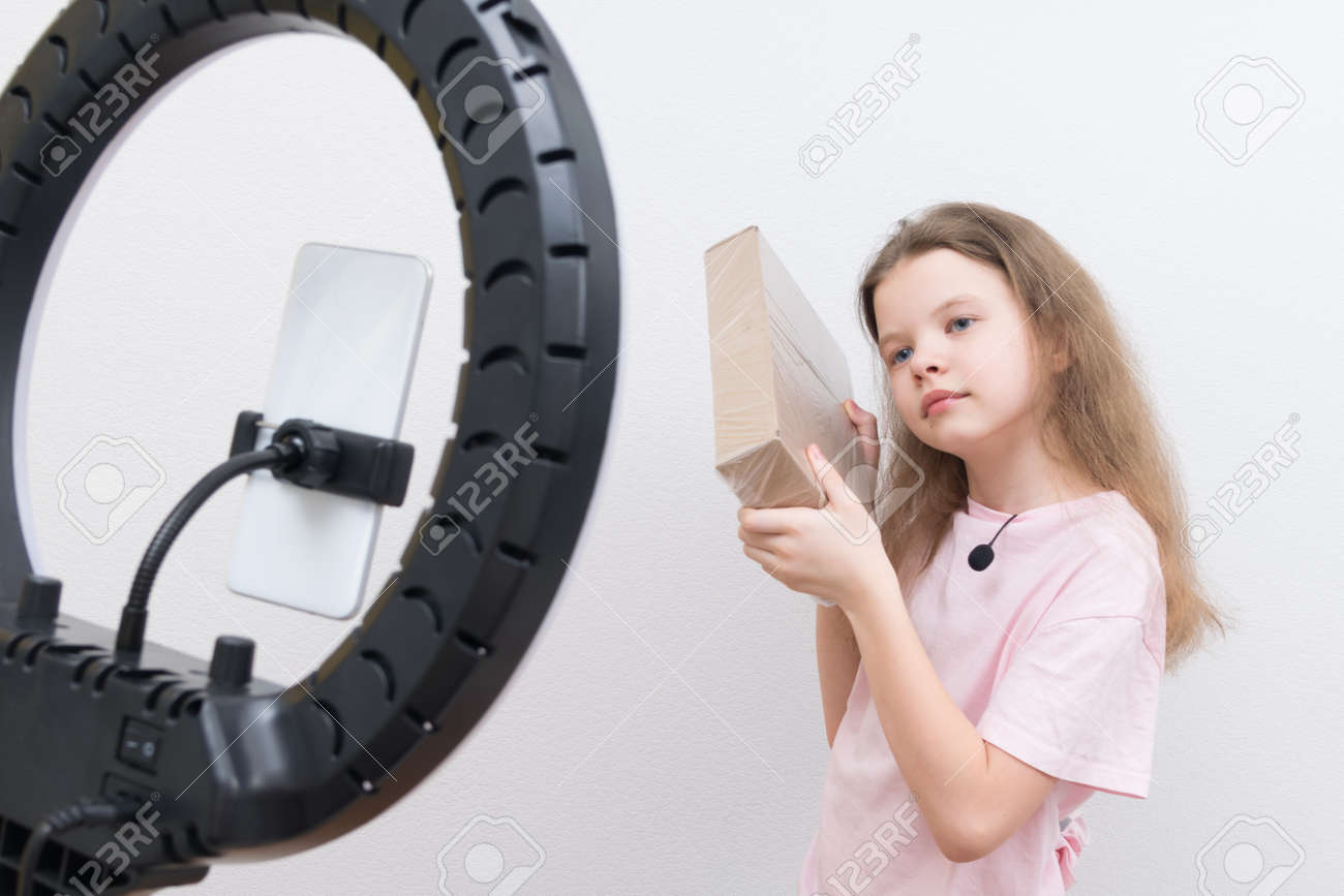 a girl blogger, in front of a circular lamp and a smartphone, makes a review of the package for unpacking - 169657127 a girl blogger, in front of a circular lamp and a smartphone, makes a review of the package for unpacking - 169657127