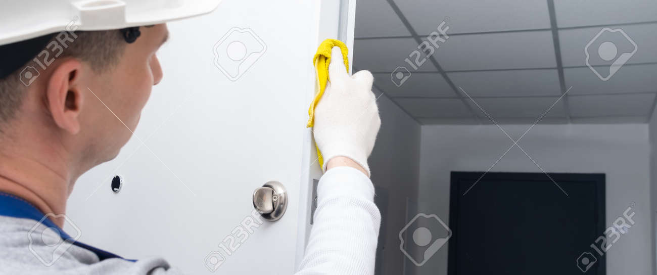 after oiling the door mechanism, the master in protective gloves and a hard hat, wipes the edges of the doors and locks with a yellow cloth - 169657145 after oiling the door mechanism, the master in protective gloves and a hard hat, wipes the edges of the doors and locks with a yellow cloth - 169657145