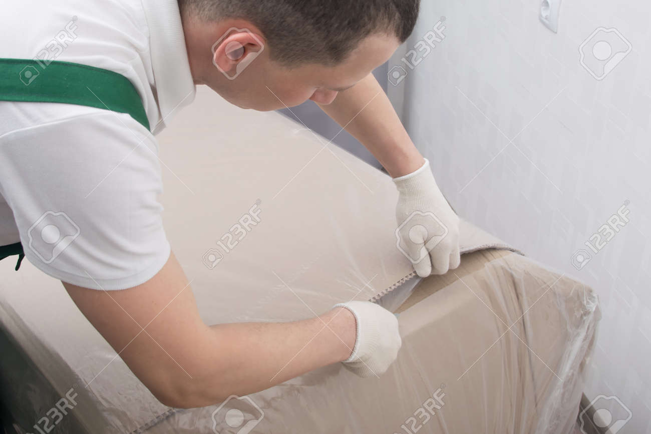 the delivery man in protective gloves, cuts the dense polyethylene, to protect the cardboard from moisture, close-up - 169657153 the delivery man in protective gloves, cuts the dense polyethylene, to protect the cardboard from moisture, close-up - 169657153