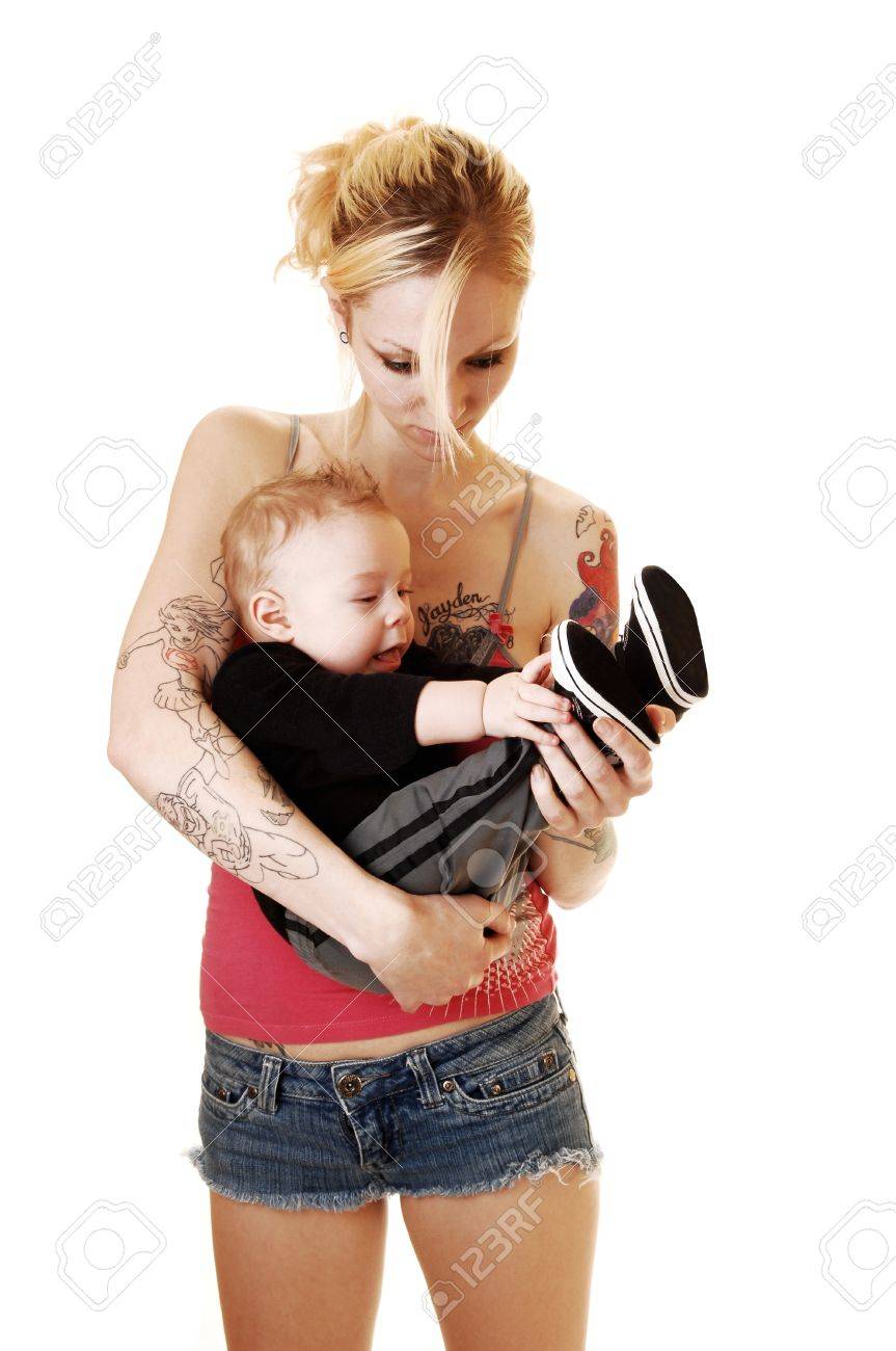 Une Mere Blonde En Short Tenant Son Bebe Dans Ses Bras Et Il Est Playingwith Ses Chaussures La Femme Avec Le Tatouage Sur Son Corps Pour Le Fond Blanc Banque D Images Et