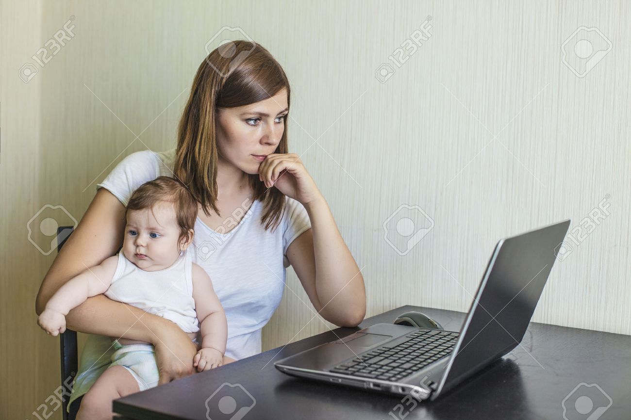 The mother of the woman with the child on hands at work behind the laptop at home - 41866876 The mother of the woman with the child on hands at work behind the laptop at home - 41866876