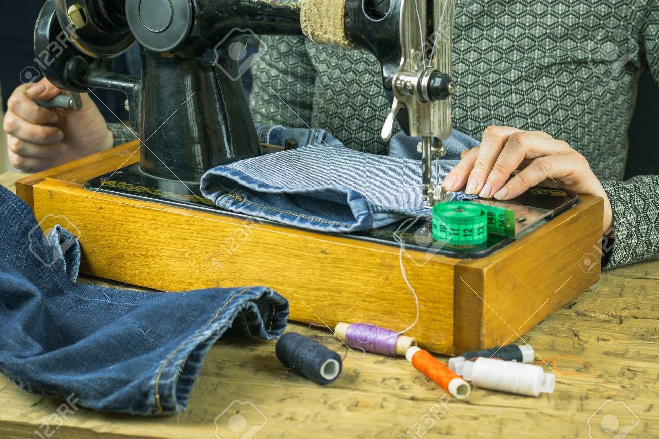 Une femme cousant des jeans sur le manuel de la machine à coudre. Le concept de production à domicile et de réparation de vêtements. Une femme cousant des jeans sur le manuel de la machine à coudre. Le concept de production à domicile et de réparation de vêtements.