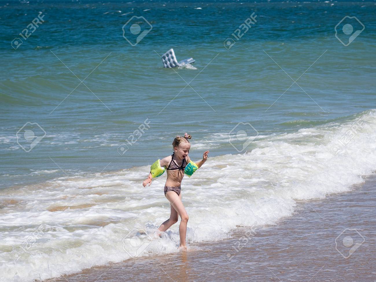 女の子は 荒れ狂う海から恐怖で逃げます 風は海に膨脹可能なマットレスを運ぶ 少女は恐怖で逃げます の写真素材 画像素材 Image
