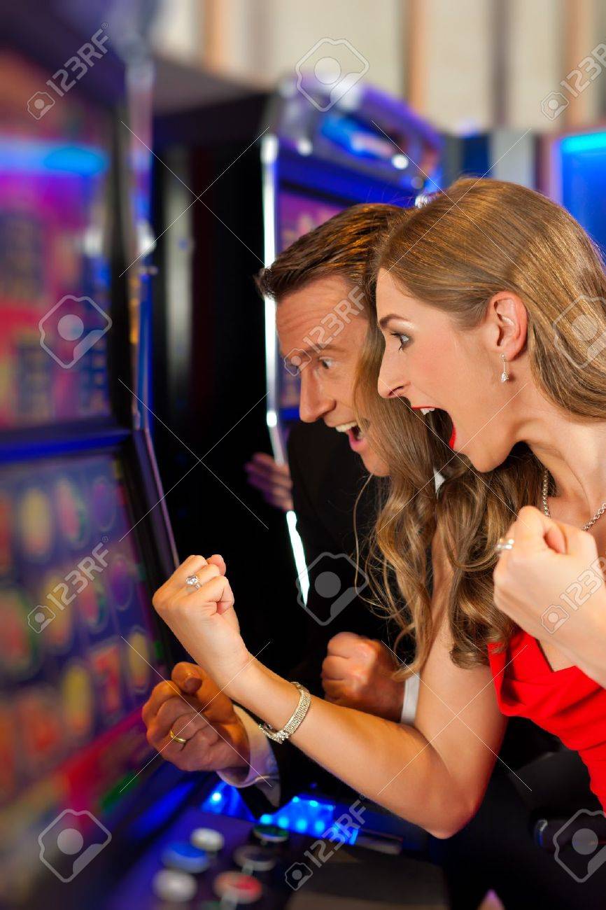 Pareja En El Casino En Una Máquina Tragamonedas Ganar Y Divertirse Fotos, Retratos, Imágenes Y Fotografía De Archivo Libres De Derecho. Image 12443394.