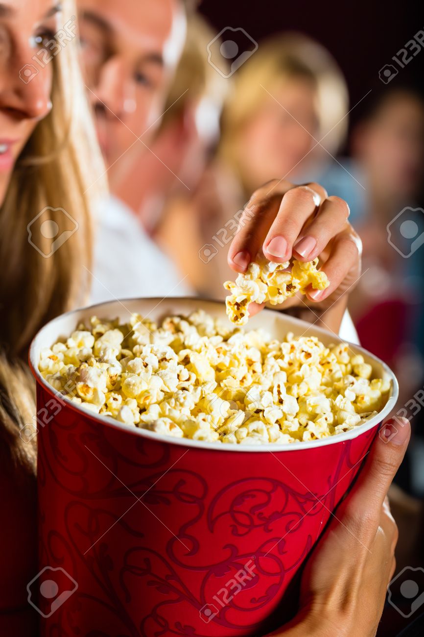 woman eating large container of popcorn in cinema or movie theater