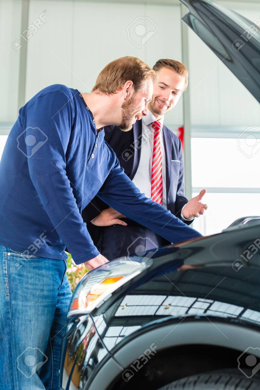 売主や車のセールスマンとクライアントまたはカーディーラーのショールームで新車 中古車のエンジンの性能のフードの下で探している男性を提示のお客様 の写真素材 画像素材 Image