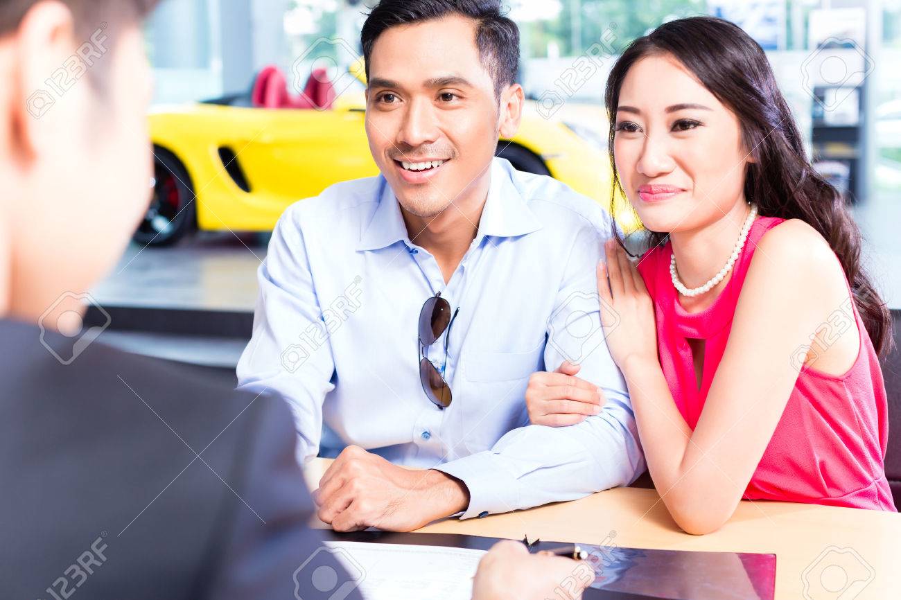 asian couple signing sales contract for car at dealership stock
