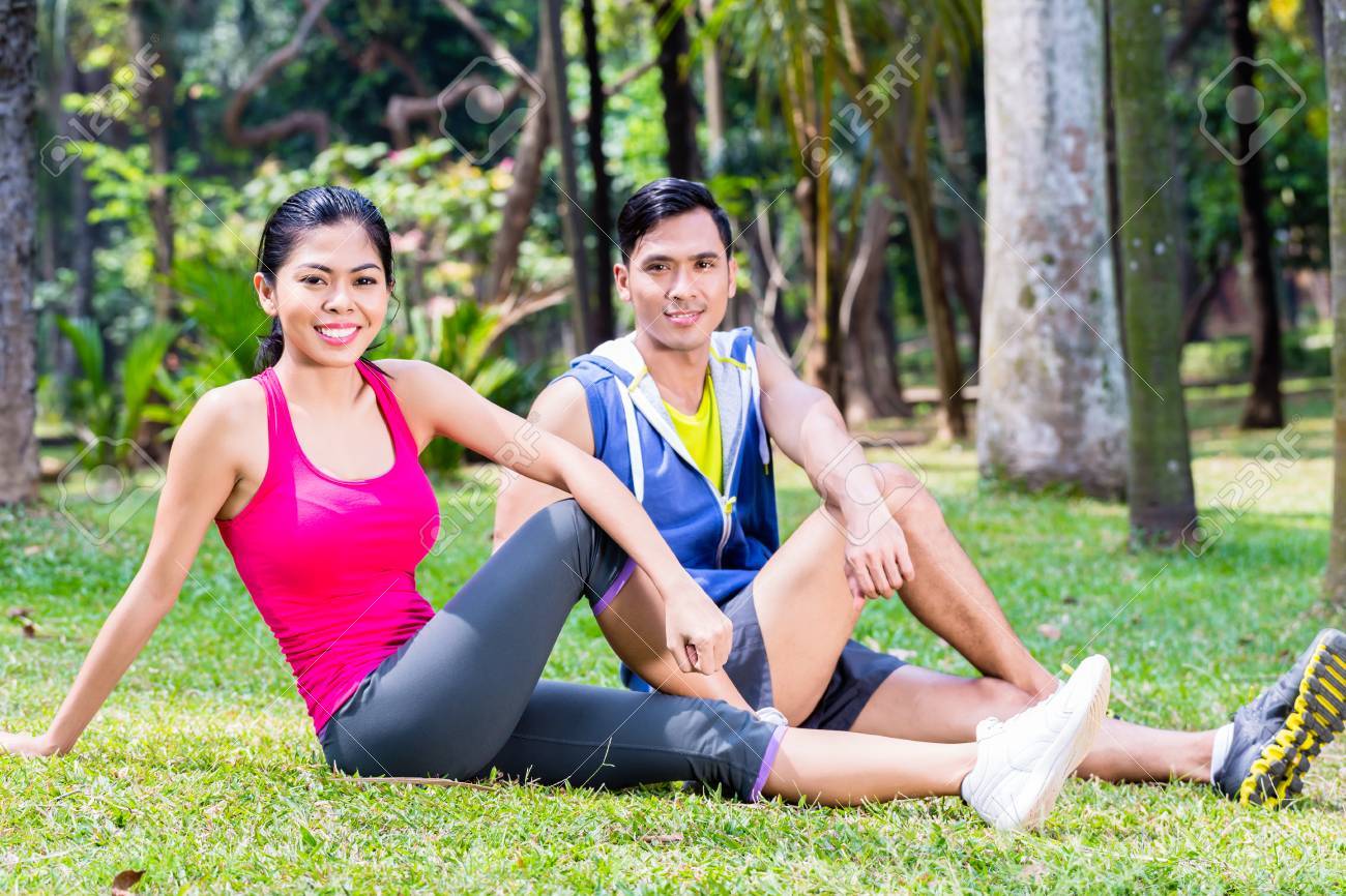 熱帯アジア公園で腹筋をしているカップル 人および女性のスポーツの芝生の上に座って運動します の写真素材 画像素材 Image