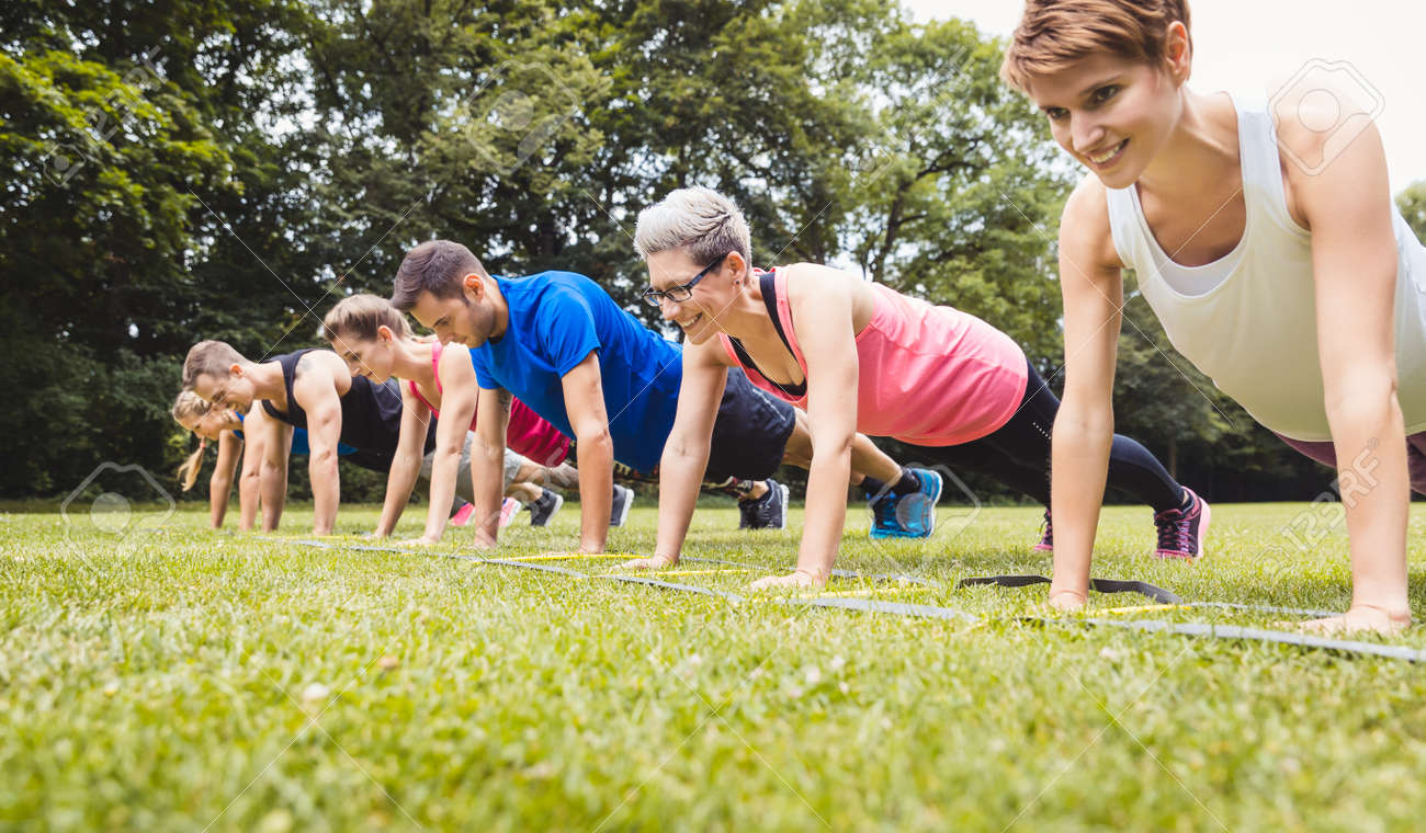 Fitness group practising push-ups in park - 168625252 Fitness group practising push-ups in park - 168625252