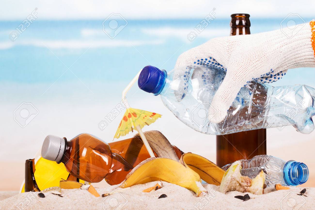Hand holding a plastic bottle on a pile of garbage in the sand background. - 67390794 Hand holding a plastic bottle on a pile of garbage in the sand background. - 67390794