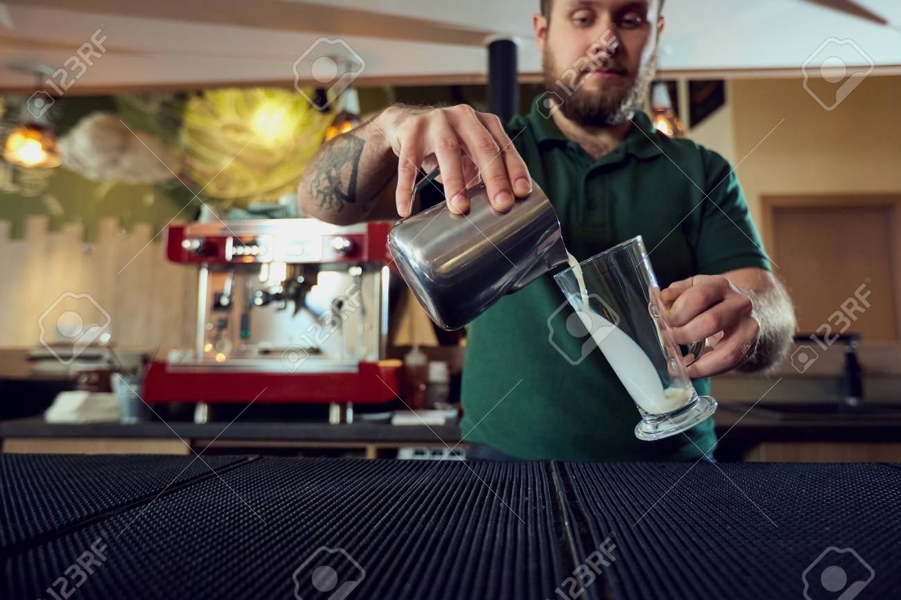 the bartender barista pours hot milk into a glass in bar cafe bartender barista