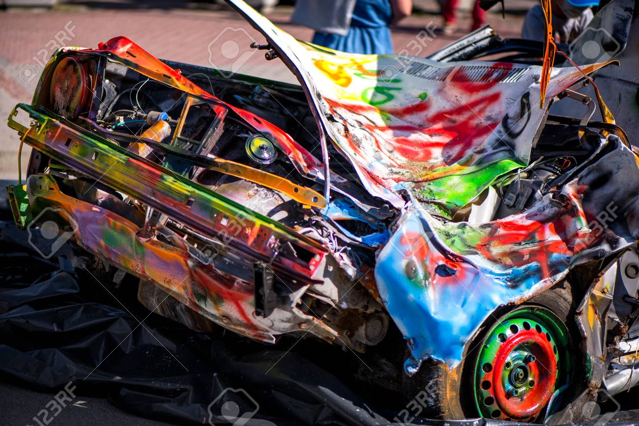 Macro Shot Of A Colorfully Painted Car, An Old Crashed, Damaged Car Wreck. Kids Are Having Fun, Making Drawings And Graffiti Art, Paint On Wreck And Tires With Green, Red, Orange, Yellow,