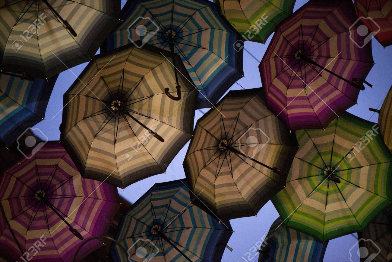 Night shot of colorful umbrellas in small street in middle of city on blue evening sky background. Romantic walk in rainy day - 119718500 Night shot of colorful umbrellas in small street in middle of city on blue evening sky background. Romantic walk in rainy day - 119718500