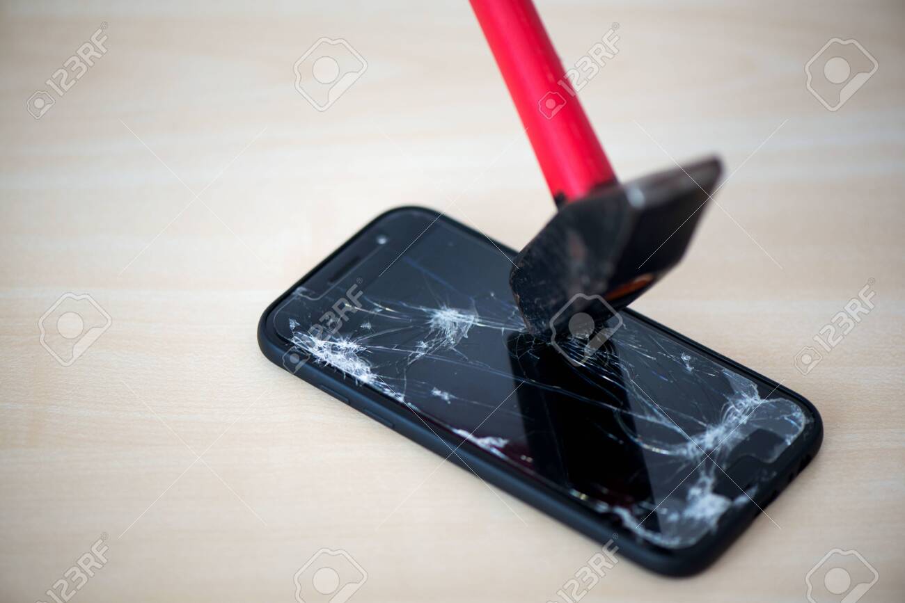 Hammer cracking on smartphone. Screen and display is destroyed, damaged and cracked. Concept of anger, rage and repairing electronic devices. Valid warranty - 119718892 Hammer cracking on smartphone. Screen and display is destroyed, damaged and cracked. Concept of anger, rage and repairing electronic devices. Valid warranty - 119718892