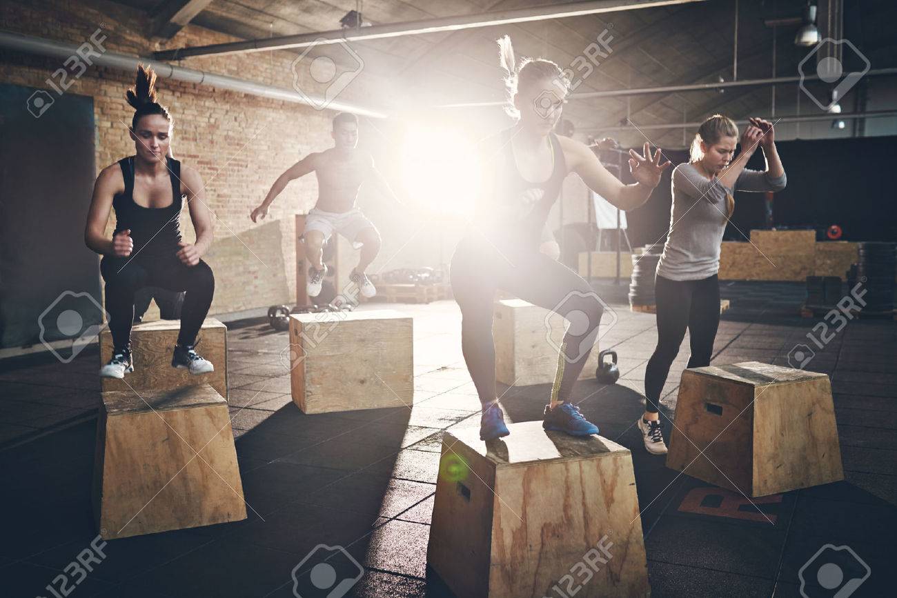 Fit young people doing box jumps as a group in a gym - 57996903 Fit young people doing box jumps as a group in a gym - 57996903