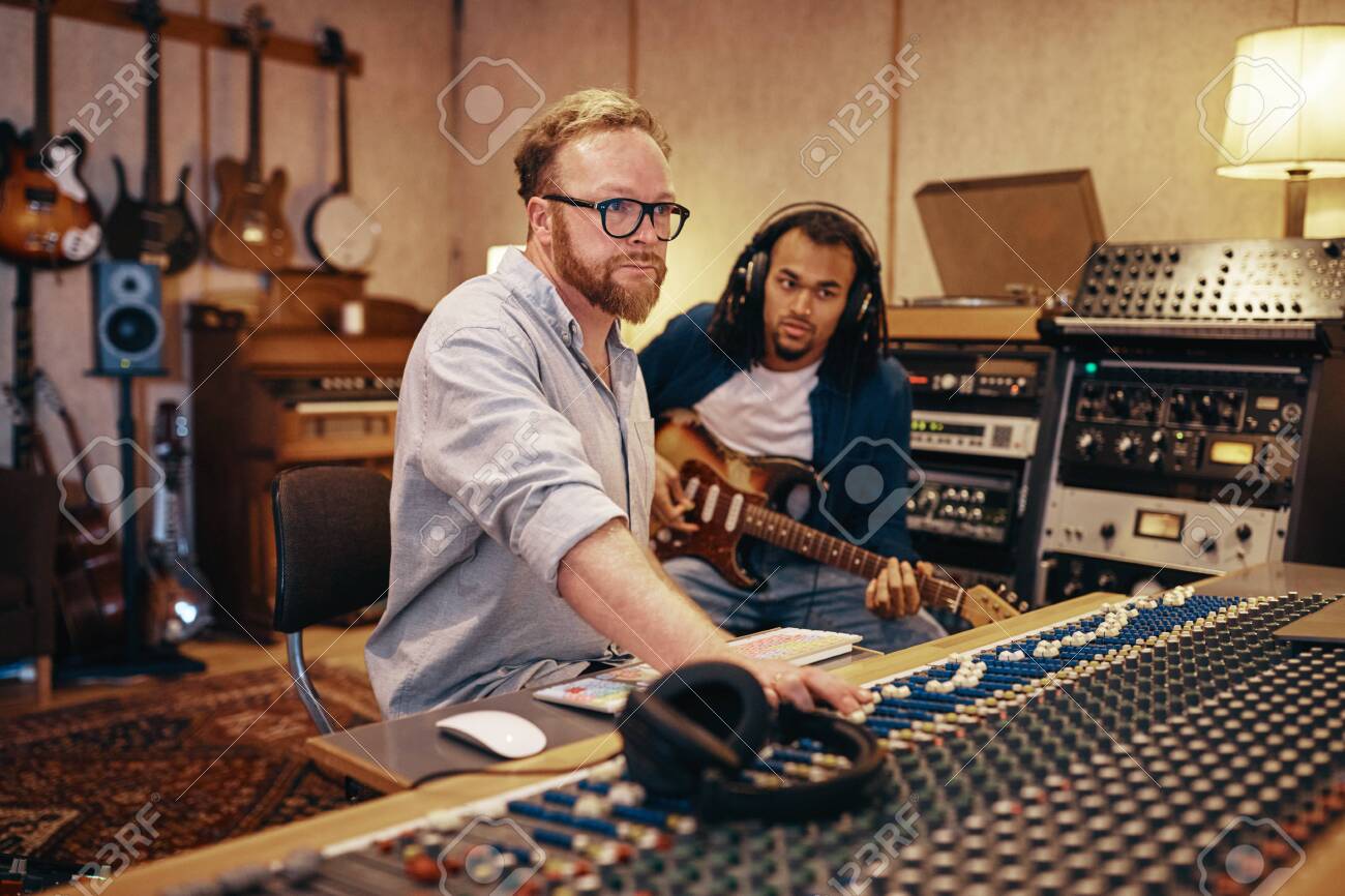 Music Producer Making Adjustments On A Soundboard With A Young African American Musician Playing Guitar In The Background Stock Photo Picture And Royalty Free Image Image 121104642